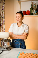 Wall Mural - Cooking sweets. Woman in blue jeans apron stands near kitchen unit and smiles