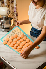 Wall Mural - Woman chef removes freshly baked halves of macarons from silicone baking sheet.