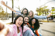 © carlesiturbe - Multi ethnic group of millennial friends taking a selfie in the street. Cheerful multiracial group of young hipsters laughing and taking a picture outside and looking at camera.