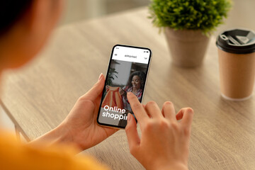 Young woman using cellphone for online shopping, searching and choosing new clothes, fashion store on screen