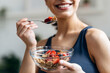 © nenetus - Athletic woman eating a healthy bowl of muesli with fruit in the kitchen at home