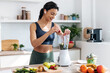 Athletic woman preparing smothie with vegetables and fruits while listening music with earphones in the kitchen at home.