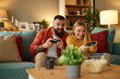 Couple sitting on couch with joysticks and playing video game in living room
