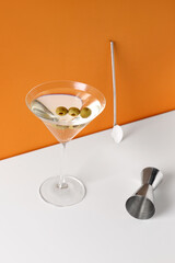 Glass of martini with olives, bar spoon and jigger on color background