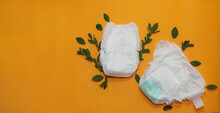Biodegradable Diapers. Eco-friendly And Disposable Diaper On An Orange Background With Green Leaves. Copy Space For Text