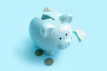 Wall Mural - Broken patched piggy bank with money on blue background. Bankruptcy concept