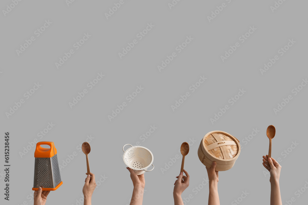 Female hands holding different kitchen utensils on grey background