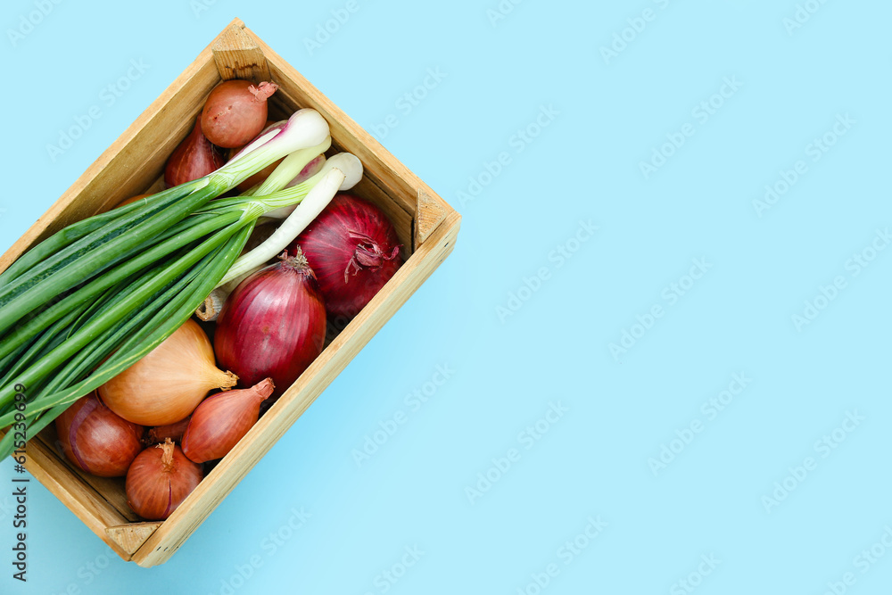 Wooden box with different kinds of onion on blue background