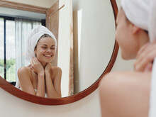 A Beauty Woman Stands In Front Of A Mirror After A Shower In A Towel On Her Head Looks At Her Reflection And Does A Face Massage Applies A Day Cream, Beauty Skin Care