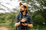 Fototapeta  - Man in nature with hat, backpack, and binoculars taking field notes