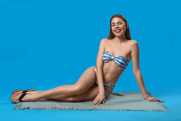 Canvas Print - Young woman in swimsuit sitting on blue background