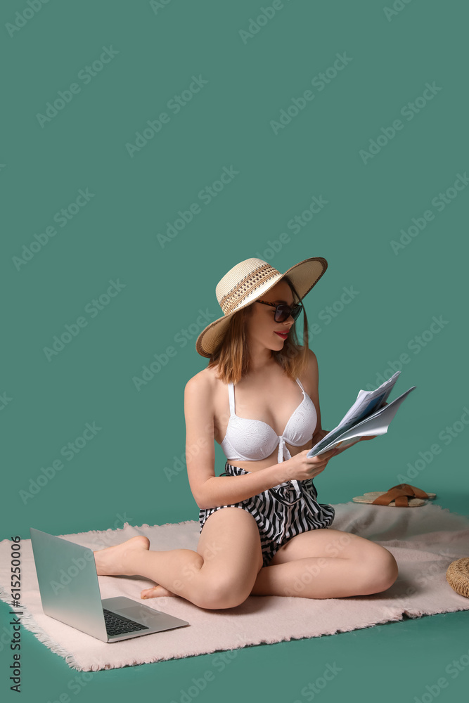 Young woman with beach accessories reading newspaper on green background