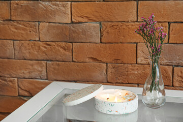 Wall Mural - Beautiful flowers and burning candle on table near brick wall in room, closeup