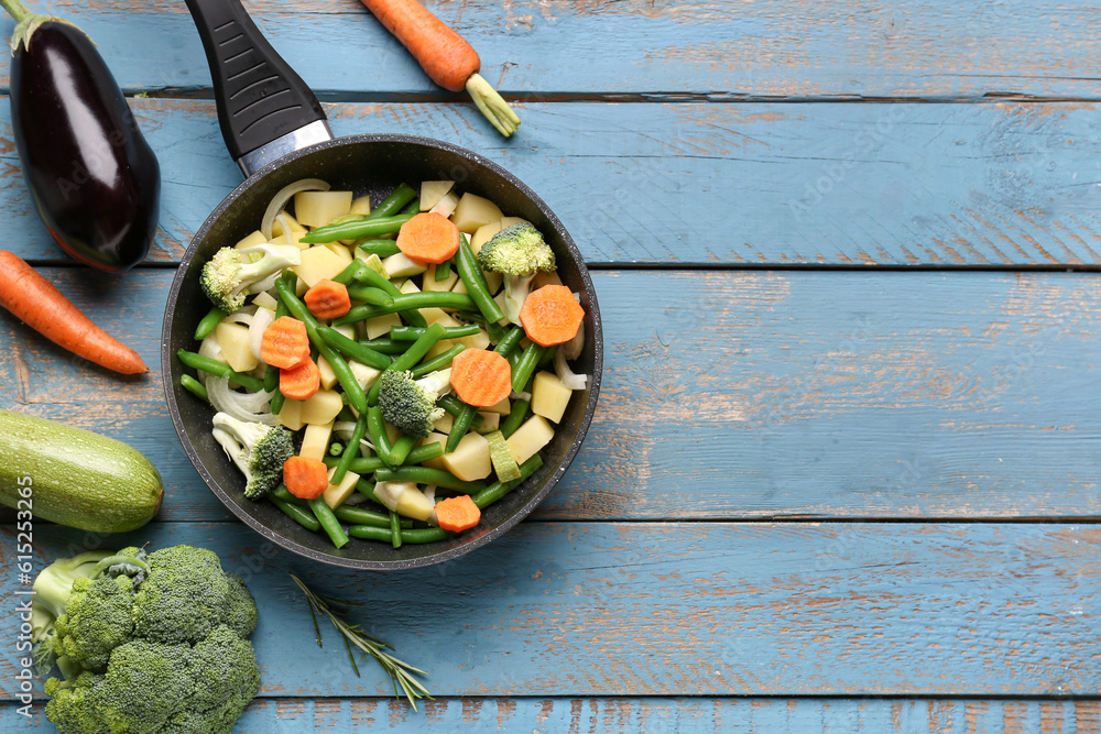 Frying pan with fresh vegetables on blue wooden background