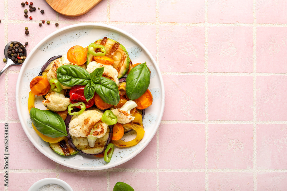 Plate with grilled vegetables and basil on pink tile background
