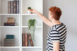 © Pixel-Shot - Young redhead man taking cactus from shelf at home