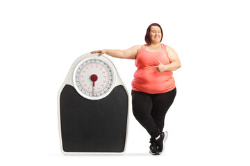 Sticker - Overweight woman in sportswear standing next to a big weight scale and pointing