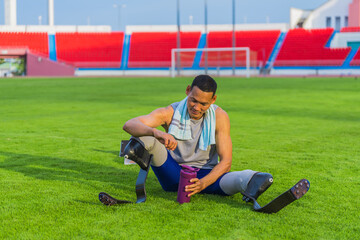 Wall Mural - Relaxed Asian Male Athlete with Prosthetic Blades Sitting on Grass Lawn Post Speed-Running Practice at Stadium