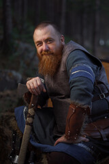 Portrait of medieval red-haired viking warrior with beard with an ax in forest