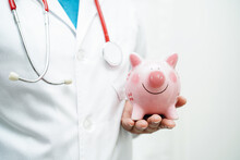 Asian Woman Doctor Holding Piggy Bank, Cost Of Treatment Or Education Concept.