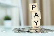 © eakgrungenerd - wooden cube block with text pay on pile of coins. spending, pay, taxes, shopping. saving money.