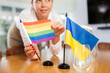 National flag of Ukraine and rainbow flag of LGBT community in hands of female office coordinator preparing meeting room for negotiations on sexual minorities rights, selective focus..