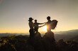 © Tinnakorn - Silhouette of celebrating life, Hikers climbing up mountain cliff. Businessman and women group hike on the peak of  rocks mountain at sunset, success, winner and leader concept.