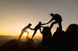 Silhouette of  Hikers climbing up mountain cliff. Climbing group helping each other while climbing up in sunset. Concept of help and teamwork.