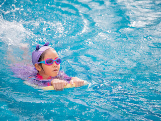 Asian child or kid girl wearing swimming suit to learning on swimming pool , learn and training swim on kick board