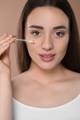 Wall Mural - Woman applying essential oil onto face on brown background, closeup