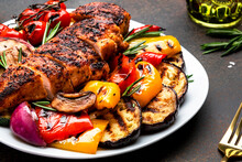 Grilled chicken fillet and vegetables salad. Colorful paprika, zucchini, eggplant, mushrooms, tomatoes, red onion with rosemary, served on plate, brown table background, top view