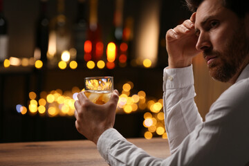 Wall Mural - Man with glass of whiskey at bar counter against blurred lights. Space for text