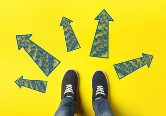 Wall Mural - Choosing future profession. Teenager standing in front of drawn signs on yellow background, top view. Arrows pointing in different directions symbolizing diversity of opportunities