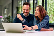 © bnenin - A smiling female employee points at a laptop screen and sitting with a male colleague.