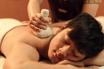 Wall Mural - Selective focus, Herbal compress on hand of masseur. Relaxation Asian man customer get service Thai herbal compress massage in beauty spa centre. Body care.