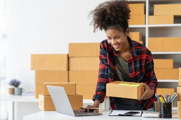 African american young woman startup business concept ecommerce business owner online on laptop Work on packing products, parcel boxes, recording customer address information for packaging delivery.