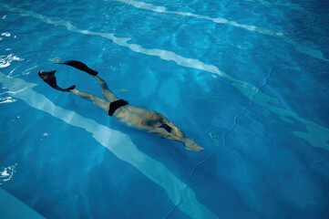 Wall Mural - Senior man wearing goggles, cap and flippers swimming in indoor pool