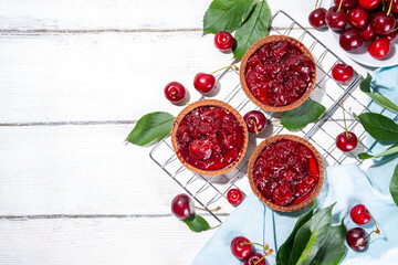 Cherry dessert tartlets. Mini tarts with cream filling and cherry topping, summer traditional pie, with fresh cherries on white wooden background