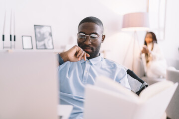Concentrated black man with book looking at laptop screen