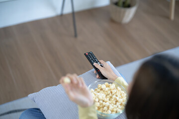 Wall Mural - Asian woman Watching smart TV and using remote controller Hand holding television audio remote control at home with the remote control television