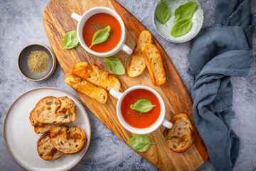Wall Mural - Homemade tomato soup with basil, toast and olive oil on a wooden cutting board.