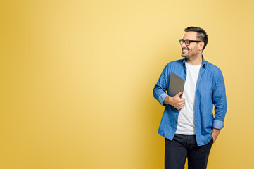 Happy male freelancer with hand in pocket holding digital tablet looking away over yellow background