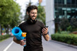 © Tetiana - Portrait of mature successful adult athlete, bearded man going to workout, coach holding fitness mat and phone, browsing online app for joint physical training