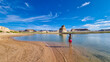 Rear view of woman walking at lakeshore looking at solitary rock formation Lone Rock in Wahweap Bay at Lake Powell, Glen Canyon Recreation Area, Page, Utah, USA. Lone rock campground in sunny summer