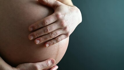 Wall Mural - Closeup of naked round belly caressed by hands of pregnant mother in underwear. Last month of pregnancy - week 36. Side angle view. Turqouise background.