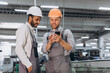 Two international male workers in overalls looking at the phone against the background of the production of aluminum PVC windows and doors