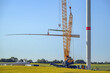 Wind turbine construction site, crane is lifting a blade to install it onto the tower, heavy industry for electricity, renewable energy and power, rural landscape, blue sky, copy space, selected focus