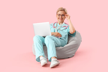 Female medical intern using laptop on pink background