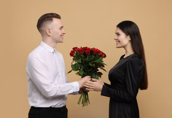 Poster - Boyfriend presenting beautiful bouquet roses to his girlfriend on beige background. Valentine's day celebration