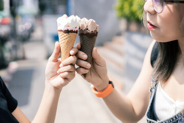 Clouse up of two young woman eating ice cream cones as they stroll along a street at city